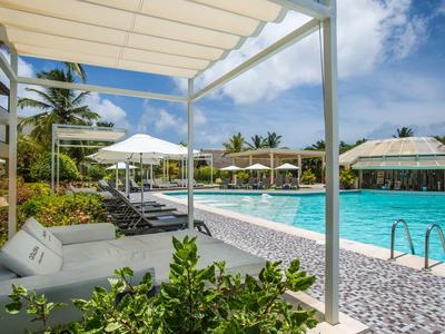 Moderne zwembadomgeving met ligstoelen, parasols en palmbomen onder blauwe lucht.