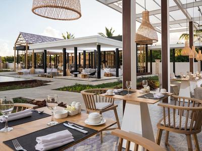 Modern restaurant buiten met houten meubels en overdekte zitgedeeltes bij daglicht.