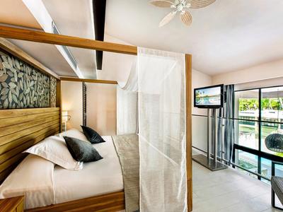 Lichte hotelkamer met houten hemelbed, witte gordijnen en grote ramen met uitzicht op de stad.