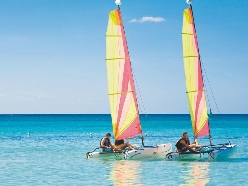 Twee kleine zeilboten met kleurrijke zeilen varen op helder blauw water.