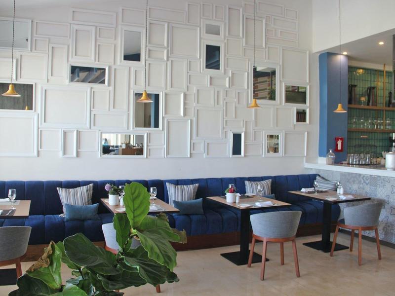 Moderne hotel eetruimte met witte muren, blauwe zitplaatsen, houten tafels en groene planten.