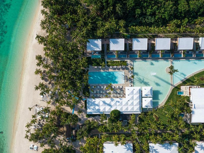Luchtfoto van een resort met zwembad, villa's aan zee en een wit zandstrand.