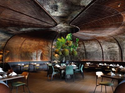 Luxuriöses, kurvig gestaltetes Restaurant mit dunklem Holz und elegant gedeckten Tischen.