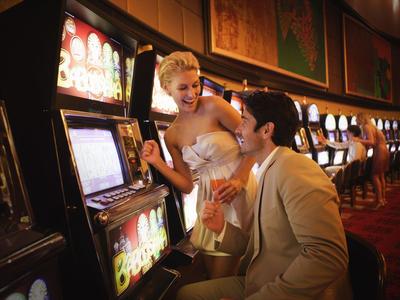 Paar spielt an Spielautomaten in einem Casino mit roten Teppichboden.