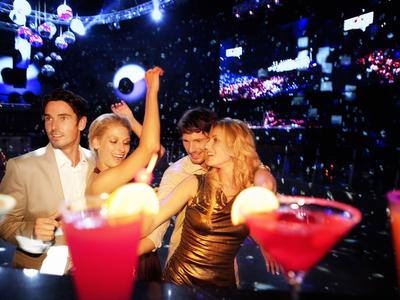 Gruppe von Freunden genießt Getränke in einer lebhaften Bar mit buntem Licht.