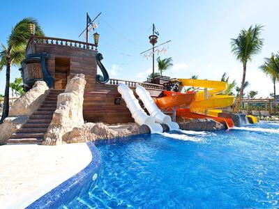 Waterpark met kleurrijke waterglijbanen en zwembadomgeving met palmbomen onder blauwe lucht.