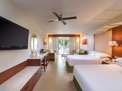 Modern hotelkamer met twee bedden, flatscreen-tv, bureau en balkon met uitzicht op groen.