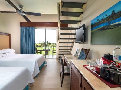 Hotelkamer met twee bedden, bureau, tv en terras met uitzicht op groene tuin