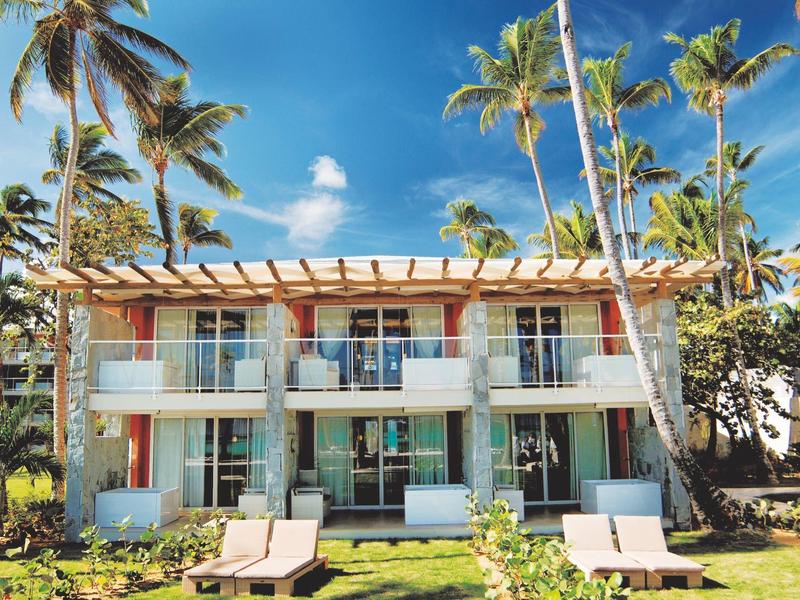 Breit wit zandstrand met palmbomen en helderblauwe zee onder een heldere lucht.