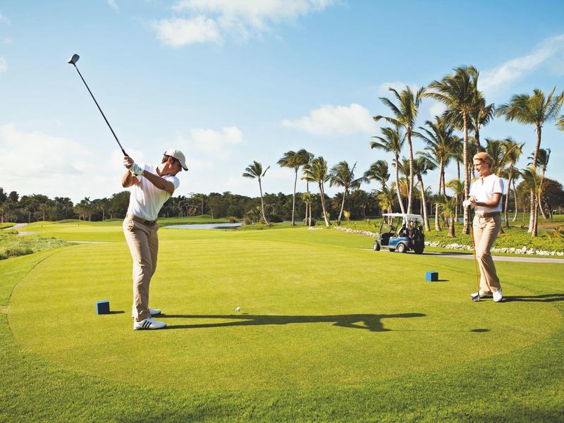 Twee mannen spelen golf op een zonnige golfbaan met palmbomen.