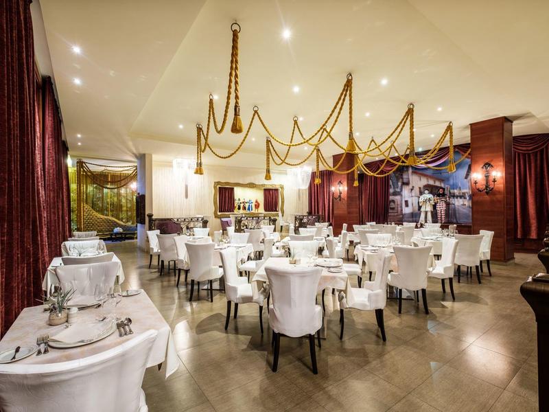 Elegant restaurant met witte tafelkleden en gouden kroonluchters aan het plafond.