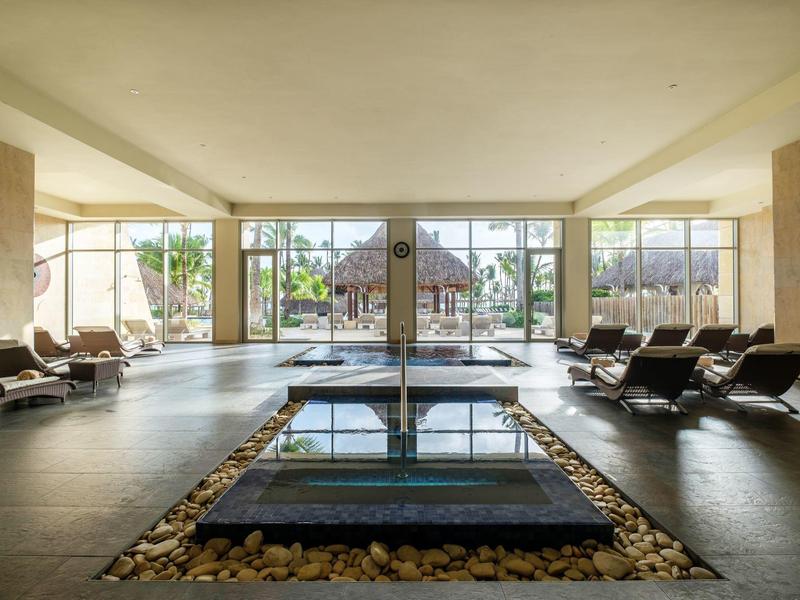 Luxe hotel spa met binnenzwembad, ligstoelen en grote glazen ramen met uitzicht op tuin.