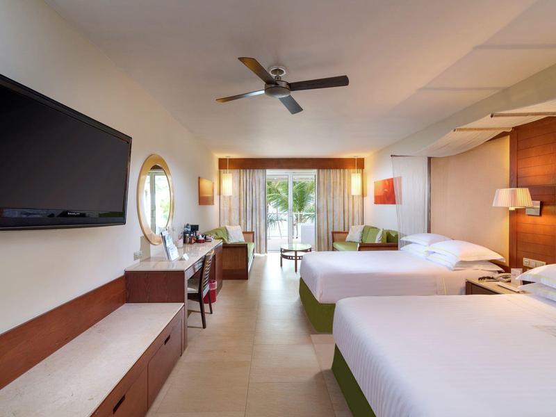 Modern hotelkamer met twee bedden, flatscreen-tv, bureau en balkon met uitzicht op groen.