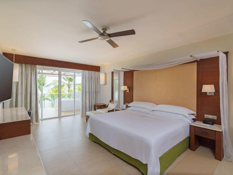 Modern hotelkamer met groot bed, plafondventilator en balkon met uitzicht op groen.