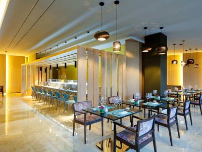 Modernes Restaurant mit hellen Wänden, Glas- und Holztischen sowie stilvollen Deckenlampen.
