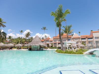 Großer Pool vor Hotelgebäude mit Palmen und klarem blauem Himmel.