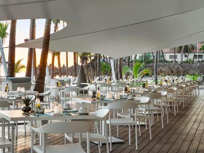 Moderner Außenbereich eines Restaurants mit weißen Tischen und Stühlen auf Holzterrasse bei Sonnenuntergang