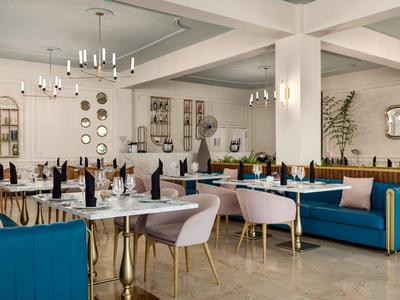 Modern eingerichteter Hotelrestaurantbereich mit blauen Sofas, rosa Stühlen und eleganten Esstischen.