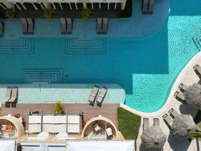 Ein blauer Pool mit Liegen, Sonnenschirmen und grünen Pflanzen in der Umgebung.