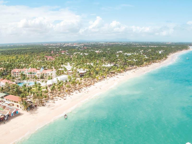 Luftaufnahme eines langen Sandstrands mit türkisfarbenem Wasser und dichtem Grün hinter dem Strand.