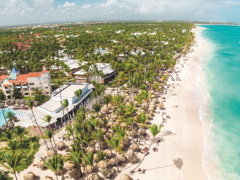 Luftaufnahme eines tropischen Strandes mit Palmen, Strandliegen und klarem blauem Wasser.
