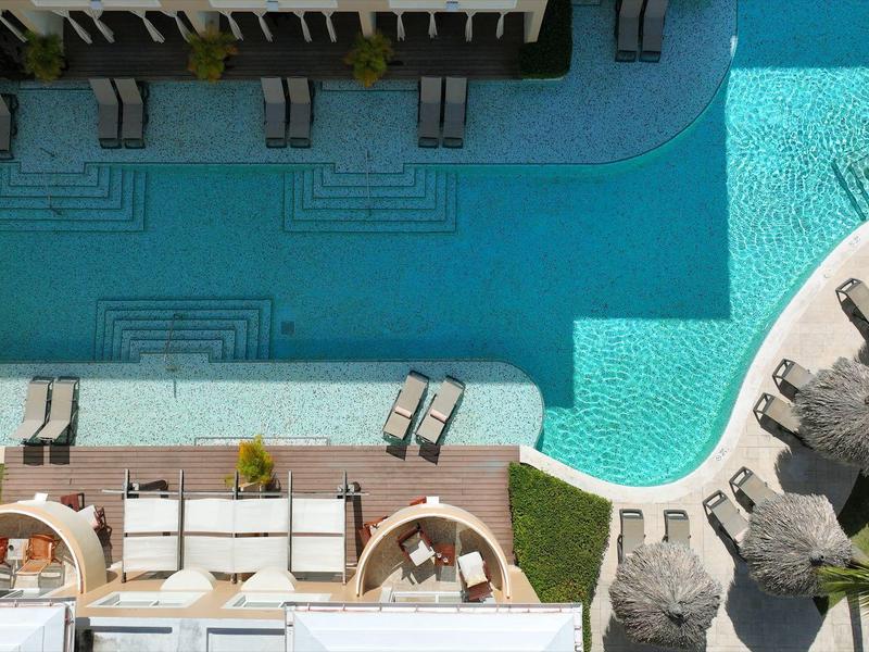 Vogelperspektive auf einen Hotelpoolbereich mit runden Sitzbereichen und Liegestühlen