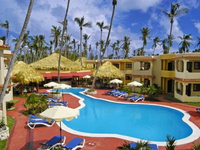 Hotelzwembad met ligstoelen, parasols en tropische begroeiing onder een blauwe lucht.