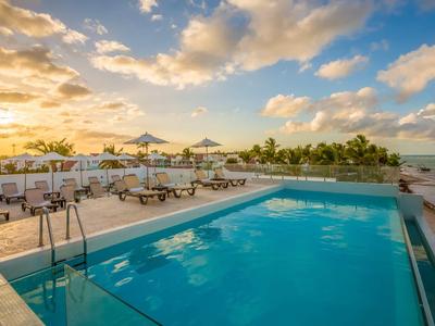 Hotelzwembad met ligstoelen en uitzicht op zee bij zonsondergang.