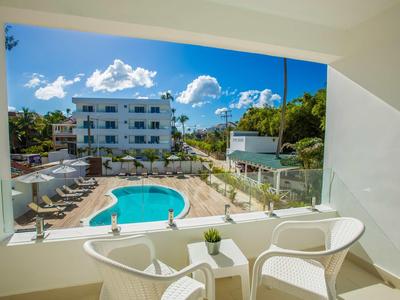 Uitzicht vanaf balkon over zwembad en meerlaagse hotelgebouw bij zonnig weer.