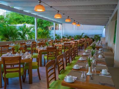 Großes, überdachtes Restaurant mit langen Holztischen, grünen Tischdecken und vielen Holzstühlen.