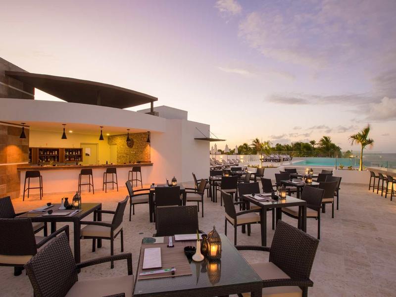 Moderne Außenbar mit zahlreichen Tischen und Stühlen auf heller Terrasse bei Dämmerung.