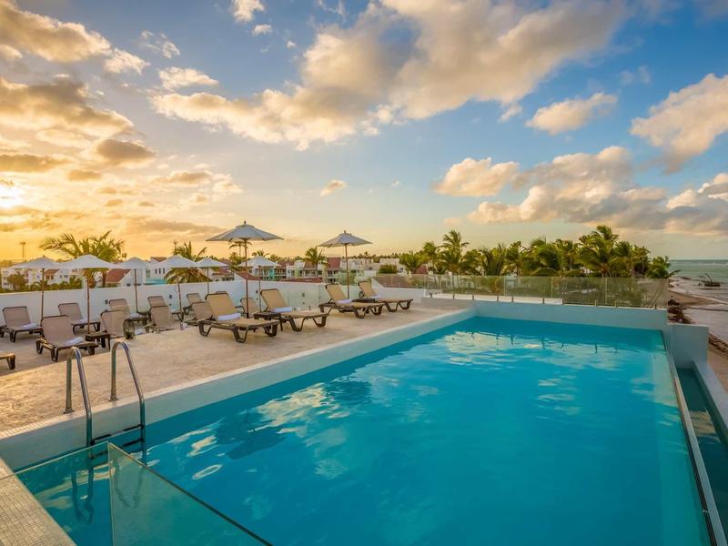 Großer rechteckiger Pool mit Liegestühlen und Sonnenschirmen bei Sonnenuntergang am Meer.