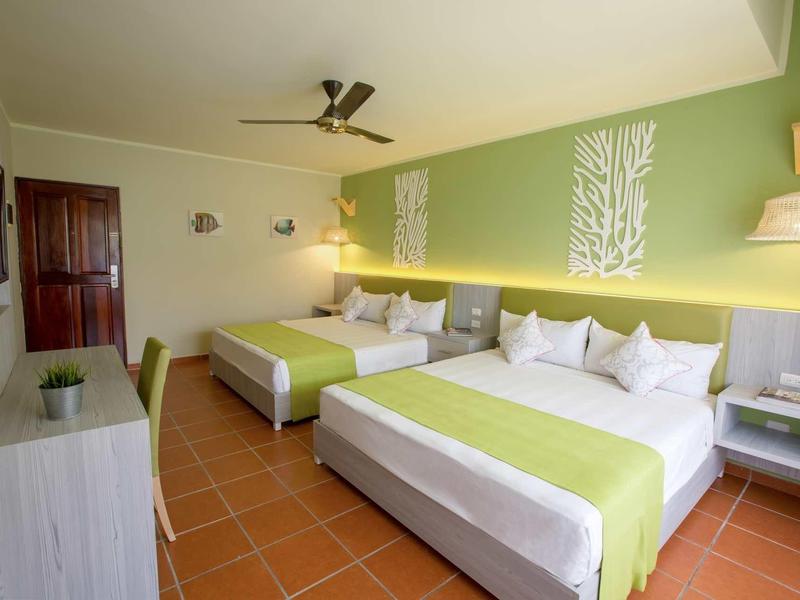 Zweibettzimmer mit grün-weißer Wand, Deckenventilator, Fliesenboden und modernen Möbeln.