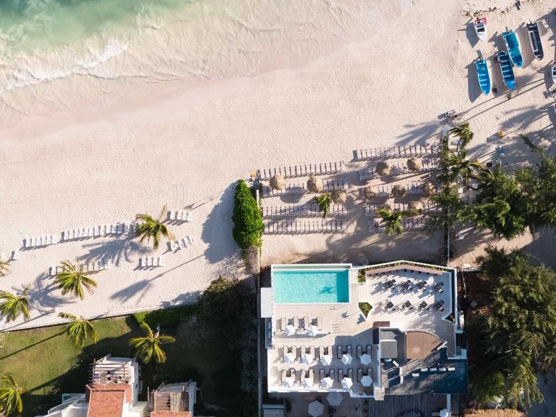 Strand mit weißem Sand, türkisfarbenem Wasser, Palmen und Poolanlagen in einer tropischen Umgebung.