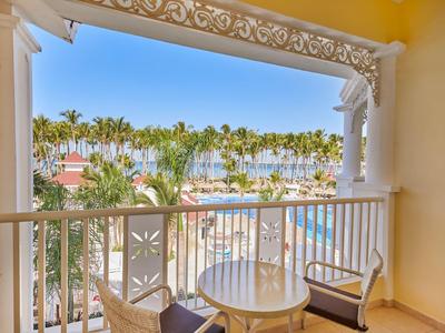 Balcon avec vue sur des palmiers, une piscine et un ciel bleu dans une station balnéaire.