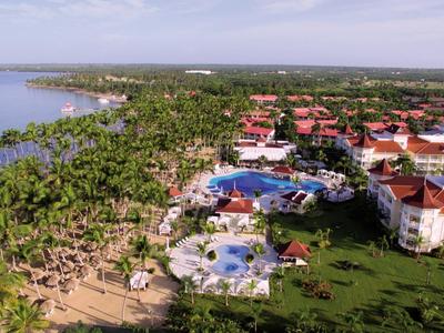 Aerial view of a tropical resort with pools, palm trees, and beach by the sea.