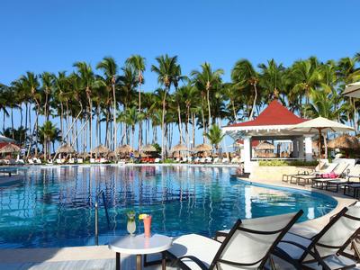 Grande piscine dans une station tropicale avec des palmiers et des chaises longues par une journée ensoleillée.