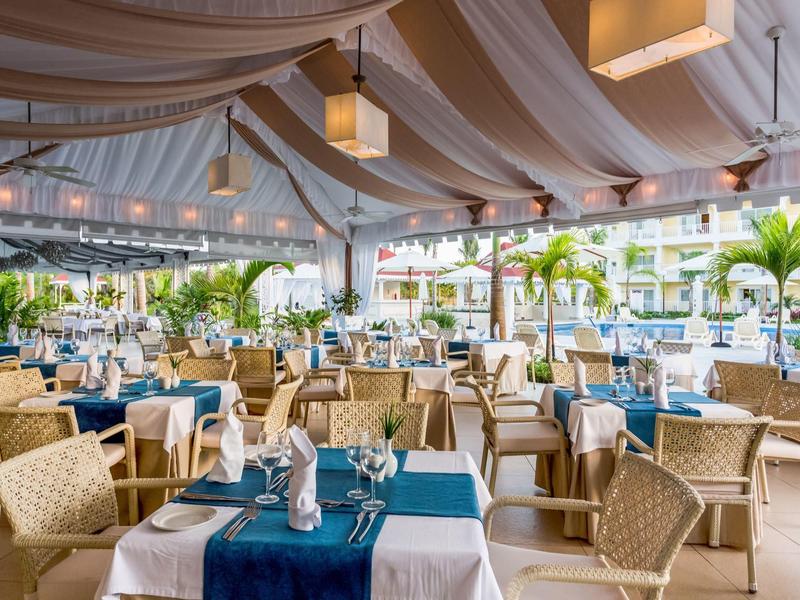 Elegant restaurant with blue table runners, set tables, and numerous plants.