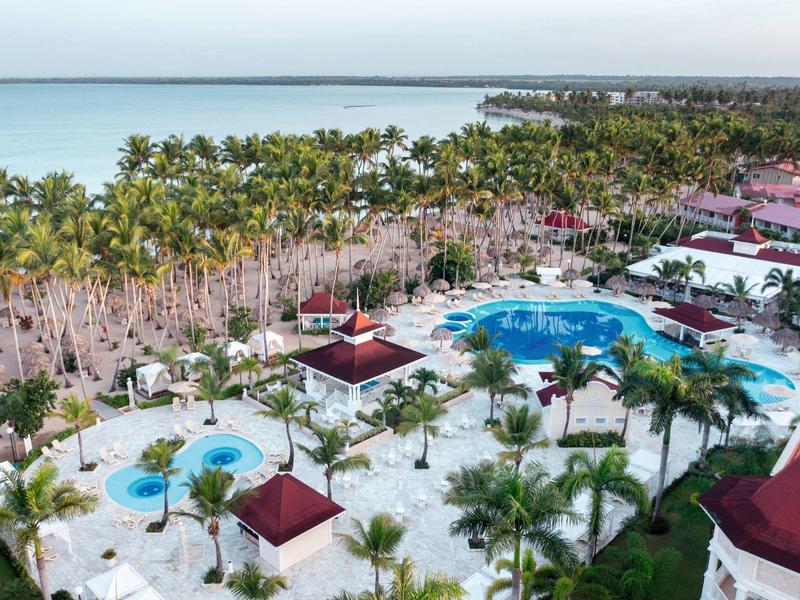Resort with pools, palm trees, and sea view under cloudy sky.