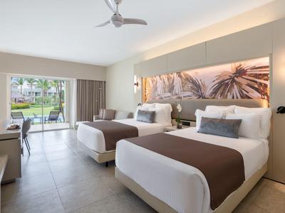 Modernes Hotelzimmer mit zwei Betten, Blick auf Garten und Terrasse durch große Glasschiebetür.