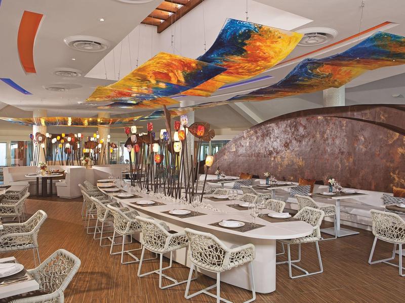 Modernes Restaurant mit bunten Deckeninstallationen und weißen Tisch- und Stuhlgruppen