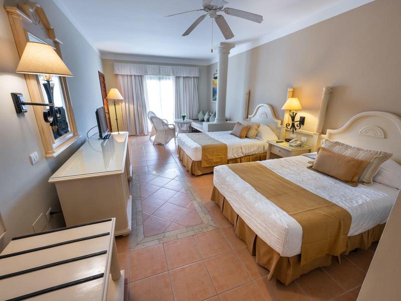 Habitación de hotel luminosa con dos camas individuales, ventilador de techo y acceso al balcón.