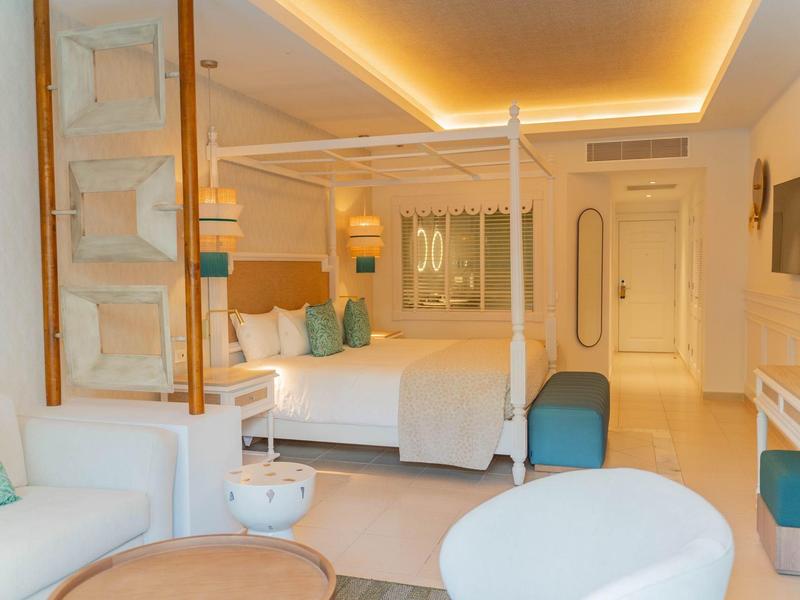 Modernes Hotelzimmer mit Doppelbett, weißen Möbeln, blauen Akzenten und indirekter Beleuchtung.