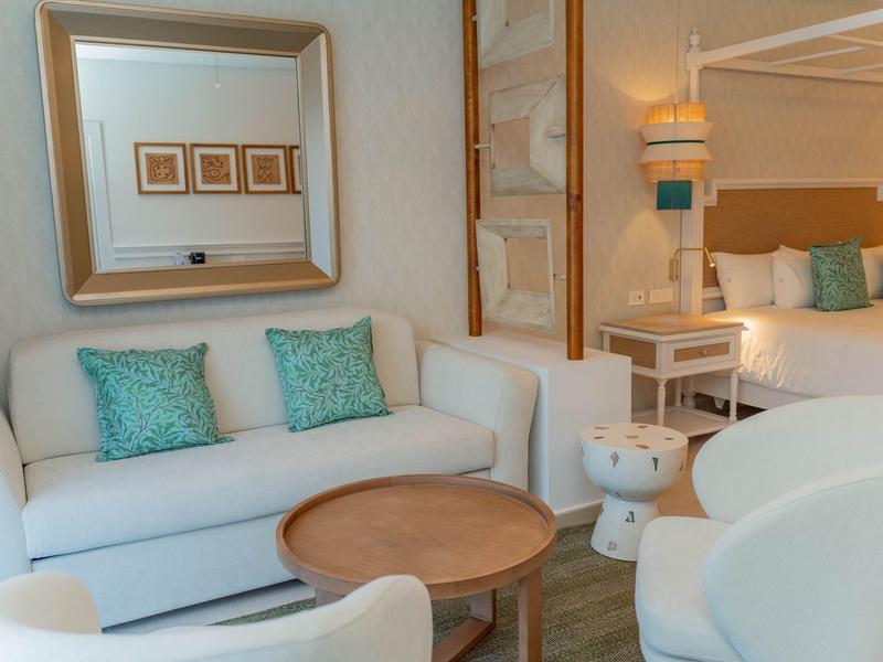 Gemütliches Wohnzimmer mit weißem Sofa, türkisfarbenen Kissen, rundem Holztisch und Stühlen.