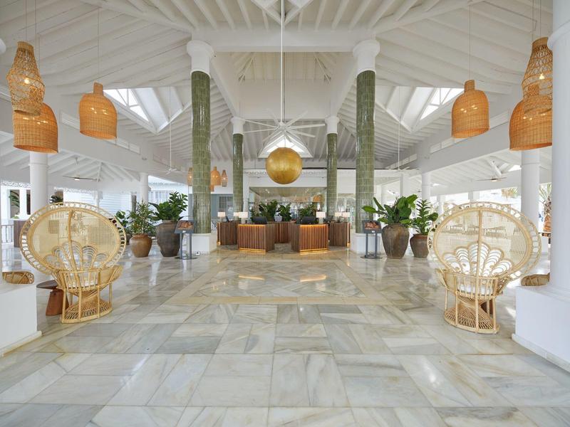 Großer heller Raum mit weißen Wänden, Marmorfußboden, Pflanzen und Rattanstühlen.