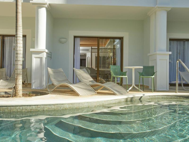 Klares Wasser im Pool vor modernen Liegestühlen und einem kleinen grünen Tisch mit zwei Stühlen.