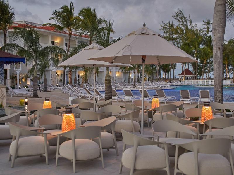 Outdoor-Café mit vielen Tischen, Stühlen und Sonnenschirmen bei Dämmerung am Hotelpool.