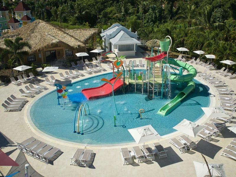 Wasserpark mit bunten Rutschen und Spritzspielen, umgeben von weißen Liegestühlen und Sonnenschirmen.