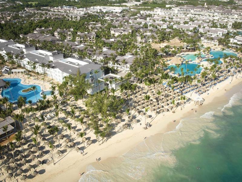 Großer Strand mit Sand, vielen Sonnenschirmen, Palmen und mehreren Hotelanlagen an türkisem Meer.