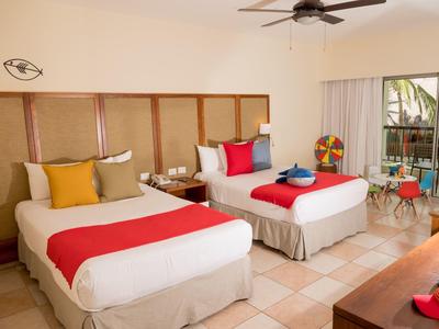 Camera d'hotel moderna con due letti singoli, cuscini colorati e terrazza con vista piscina.